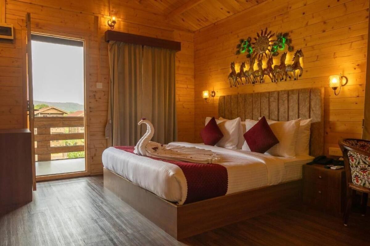 A wooden room with a bed, a wall-mounted light fixture, and a view through a door.