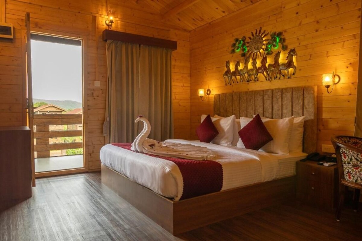 A wooden room with a bed, a wall-mounted light fixture, and a view through a door.