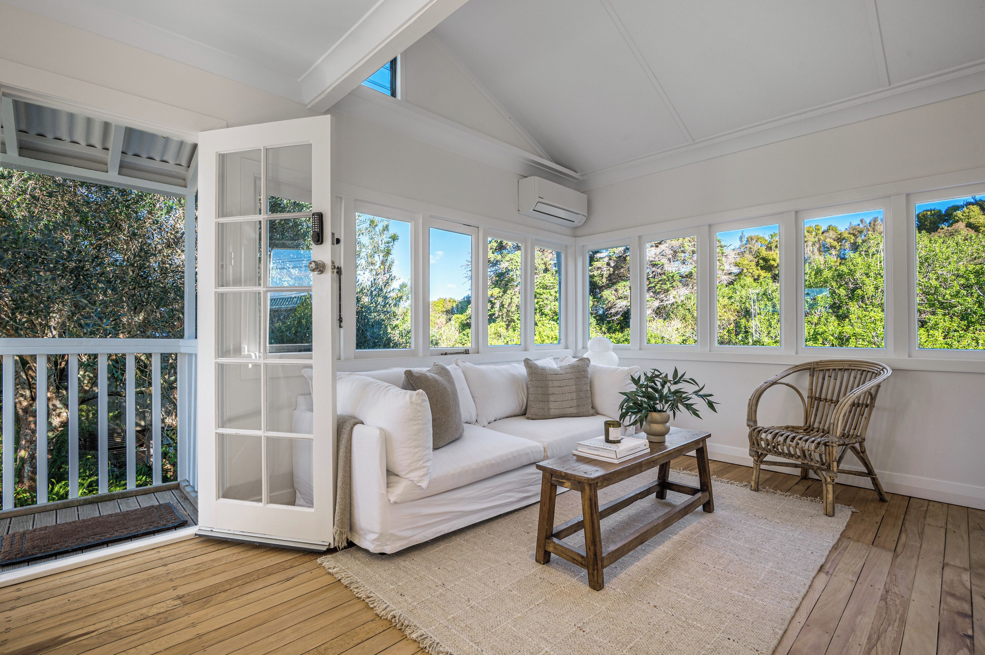 A sunlit room with a white sofa, a wooden coffee table, and a wicker chair.