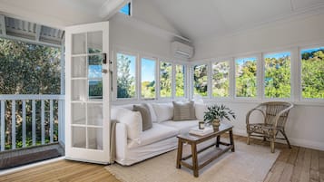 Una habitación iluminada por el sol con un sofá blanco, una mesa de centro de madera y una silla de mimbre.