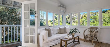 A sunlit room with a white sofa, a wooden coffee table, and a wicker chair.