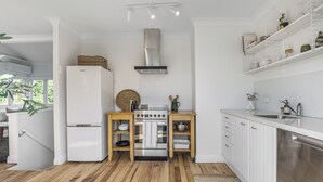A modern kitchen with white cabinetry, a stainless steel range hood, and wooden flooring.