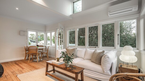 A spacious living room with a white sofa, wooden coffee table, and a dining area with chairs and a table.