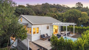 A modern house with a covered patio, a swimming pool, and a view of the surrounding forest.