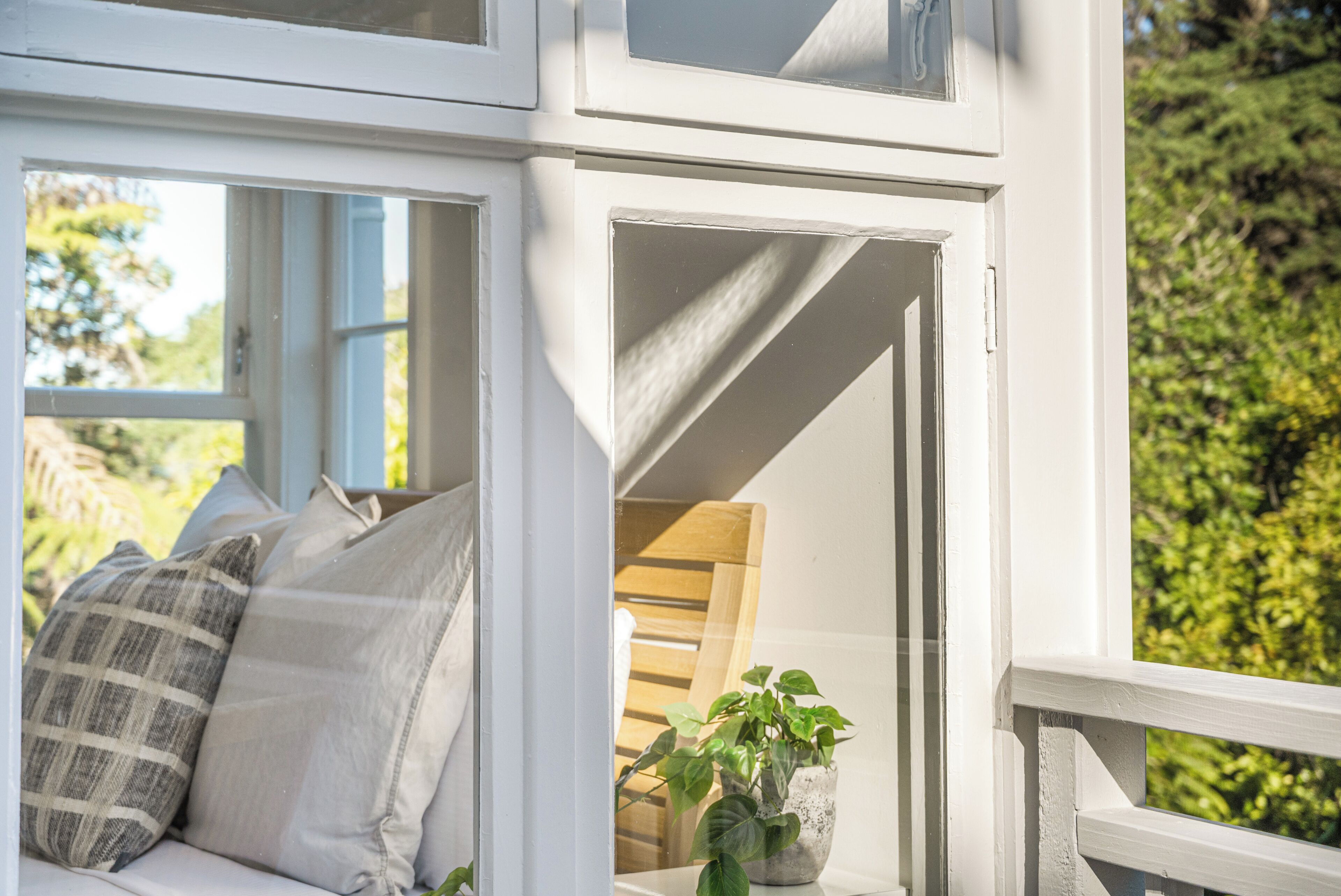Una habitación con ventana, una cama con almohadas, un banco de madera y una planta en maceta.