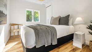 A bedroom with a bed, bedside table, lamp, and a view of greenery outside.