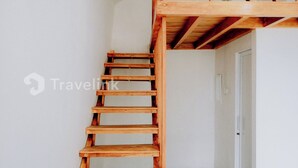 Un escalier en bois mène à une mezzanine aménagée en espace nuit, dont le plafond présente un motif géométrique.