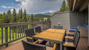 Une terrasse dotée d’une table en bois et de chaises en osier, offrant une vue sur un paysage montagneux.