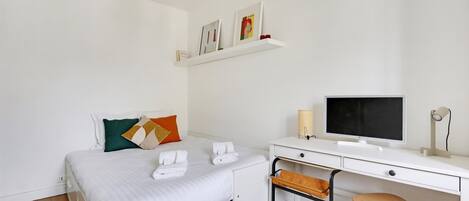 Una habitación de hotel con una cama, un escritorio con computadora, una silla y una estantería con fotografías.