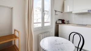 A compact kitchen with a window, a radiator, a small table, and a chair. - A Canal St Martin Lovely Room (Paris)