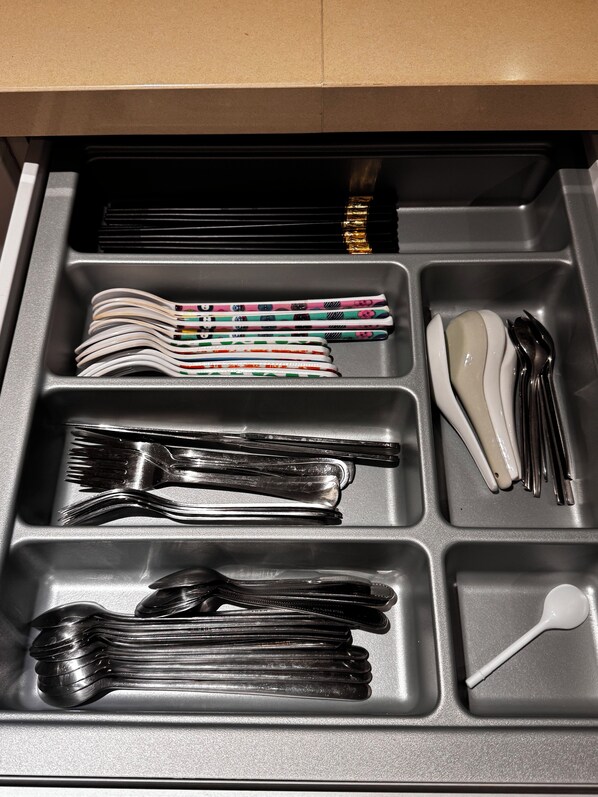 A drawer with compartments containing various utensils, including forks, spoons, and a white ladle.