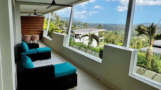 Un balcon offrant une vue sur un paysage montagneux, un ventilateur de plafond et un coin salon avec des coussins.