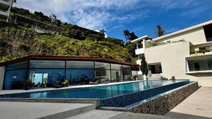 Un bâtiment moderne doté d’une piscine, entouré d’une végétation luxuriante et surplombé d’un ciel bleu azur.