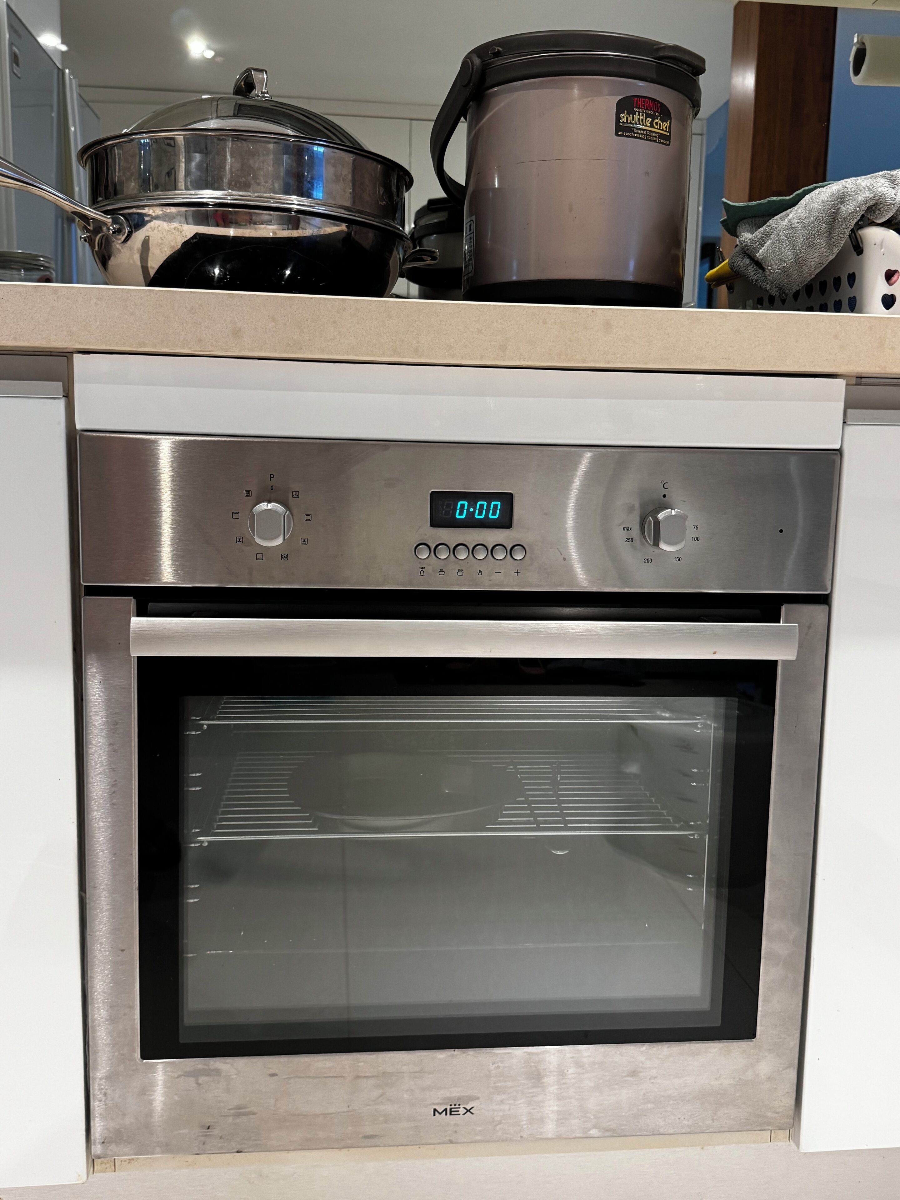Uma cozinha com forno, relógio digital e uma panela sobre o balcão.