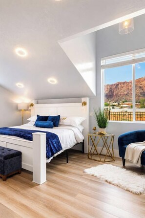 A bedroom with a bed, a side table, a chair, a window with a view, and a ceiling light.
