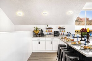 A modern kitchen with white cabinets, a marble countertop, and a view of a desert landscape.