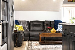 A living room with a black leather sofa, a wooden coffee table with a vase and flowers, and a patterned rug.