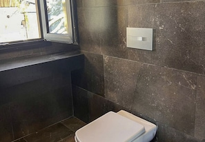A bathroom with dark tiled walls, a white toilet, and a window.