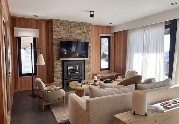 A modern living room with a stone fireplace, a flat-screen TV mounted on the wall, a sofa set, a coffee table, and a lamp.