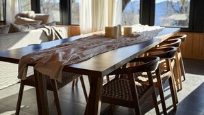 Ein Essbereich mit Holztisch, Stühlen und Blick ins Freie durch große Fenster.