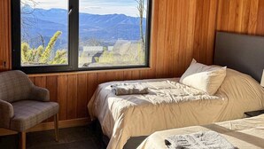 Ein Schlafzimmer mit zwei Betten, einem Sessel und einem großen Fenster mit Blick auf die Berge.
