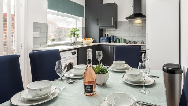 A modern kitchen with grey cabinets, a built-in stove, and a dining area set for a meal. - Cozy 4 bedroom in Aintree -Liverpool Free Parking, Super fast Wifi Internet. (Bootle)
