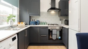 A compact kitchen with dark cabinets, a white refrigerator, and a window providing natural light. - Cozy 4 bedroom in Aintree -Liverpool Free Parking, Super fast Wifi Internet. (Bootle)