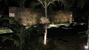 A nighttime outdoor area with a palm tree, lounge chairs, and a stone wall. - A3 - Sea view - Soleil des Canonniers (Trou-aux-Biches)