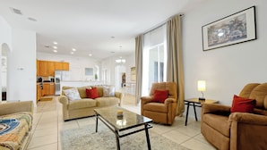 Amplia sala de estar con sofá, sillones, una mesa de centro y un comedor al fondo.