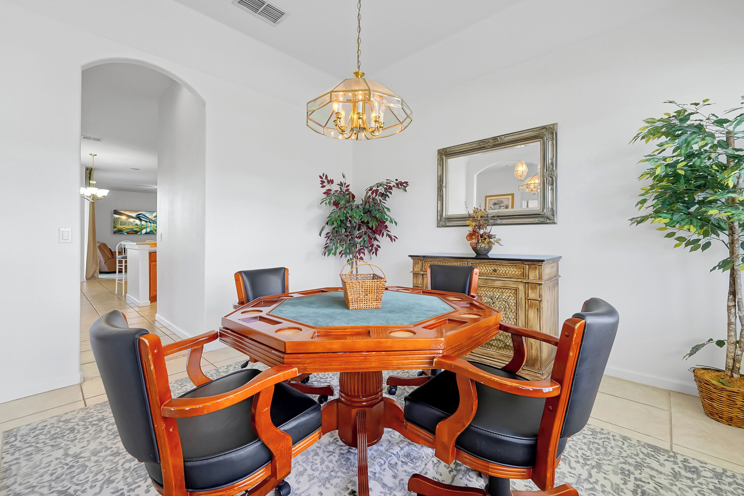 A dining area with a round wooden table, black chairs, a chandelier, a mirror, and a potted plant.