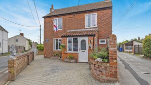 A two-story brick house with a white door and windows, a small garden with plants, and a statue on the left. - 3 bedroom accommodation in Beccles (Beccles)