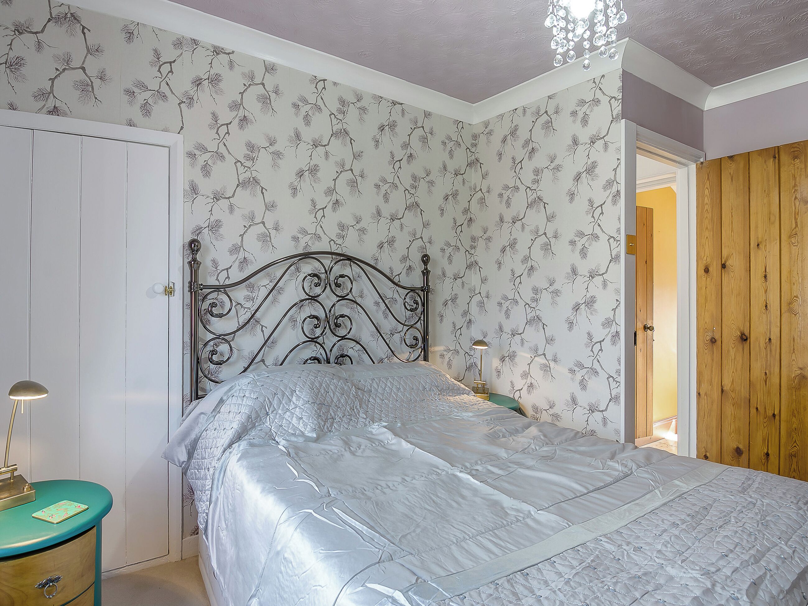 Un dormitorio con cama, mesita de noche, lámpara, armario de madera y una puerta.