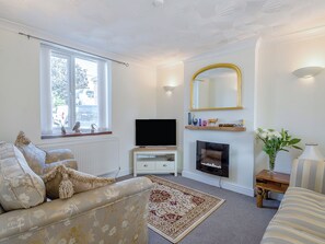 Ein Wohnzimmer mit Sofa, Fernseher, Kamin und einem Fenster mit Blick ins Freie.