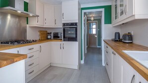 A compact kitchen with white cabinets, a wooden countertop, a stove, an oven, and a coffee maker. - 3 bedroom accommodation in Beccles (Beccles)