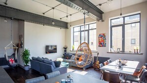 A modern living room with a sofa set, a dining table with chairs, a hanging chair, and a TV mounted on the wall. - New York Style Loft Apartment (Leith)