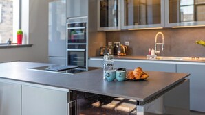 A modern kitchen with a central island, stainless steel appliances, and a window with a view of the city. - New York Style Loft Apartment (Leith)