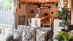 Una habitación acogedora con un sofá de mimbre, un cojín con motivos de mapa, una zona de bar de madera y una planta en maceta.