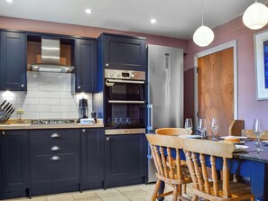 Une cuisine moderne avec des meubles de rangement aux couleurs sombres, un four encastré et un réfrigérateur en acier inoxydable.