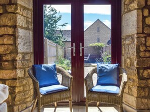A room with a stone wall, two wicker chairs with cushions, and a glass door leading outside.