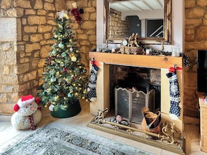 Un muro de piedra, un árbol de Navidad decorado, una chimenea con calcetines navideños y un peluche.