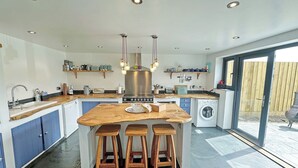 Eine moderne Küche mit einer zentralen Kochinsel, Barhocker, einer integrierten Waschmaschine und einem großen Fenster.