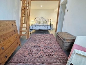 A bedroom with a bed, wooden dresser, a patterned rug, and a suitcase.
