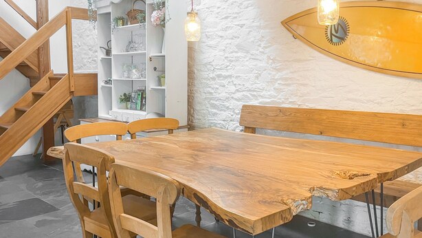 Ein Holzespeisesaal mit Stühlen, eine weiße Wand mit strukturierter Oberfläche und eine Treppe mit Holzgeländern.
