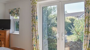 A bedroom with a bed, a TV on a wooden dresser, and a sliding glass door leading to a garden. - A spacious holiday retreat with private, enclosed garden, nestled within St. (Padstow)