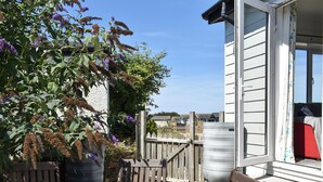A wooden deck with a table set for tea, surrounded by lush greenery and a view of a white building with a window. - A spacious holiday retreat with private, enclosed garden, nestled within St. (Padstow)