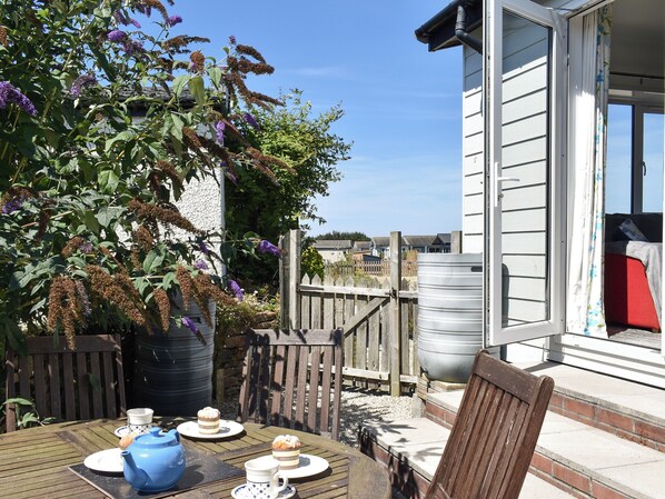 Une terrasse extérieure avec une table préparée pour le thé, une clôture en bois et un bâtiment doté d’une fenêtre.