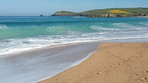 A beach with clear blue water, a sandy shore, and a distant rocky coastline. - A spacious holiday retreat with private, enclosed garden, nestled within St. (Padstow)