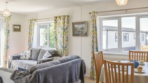 A cozy living room with a sofa, a dining table with chairs, and large windows with curtains. - A spacious holiday retreat with private, enclosed garden, nestled within St. (Padstow)