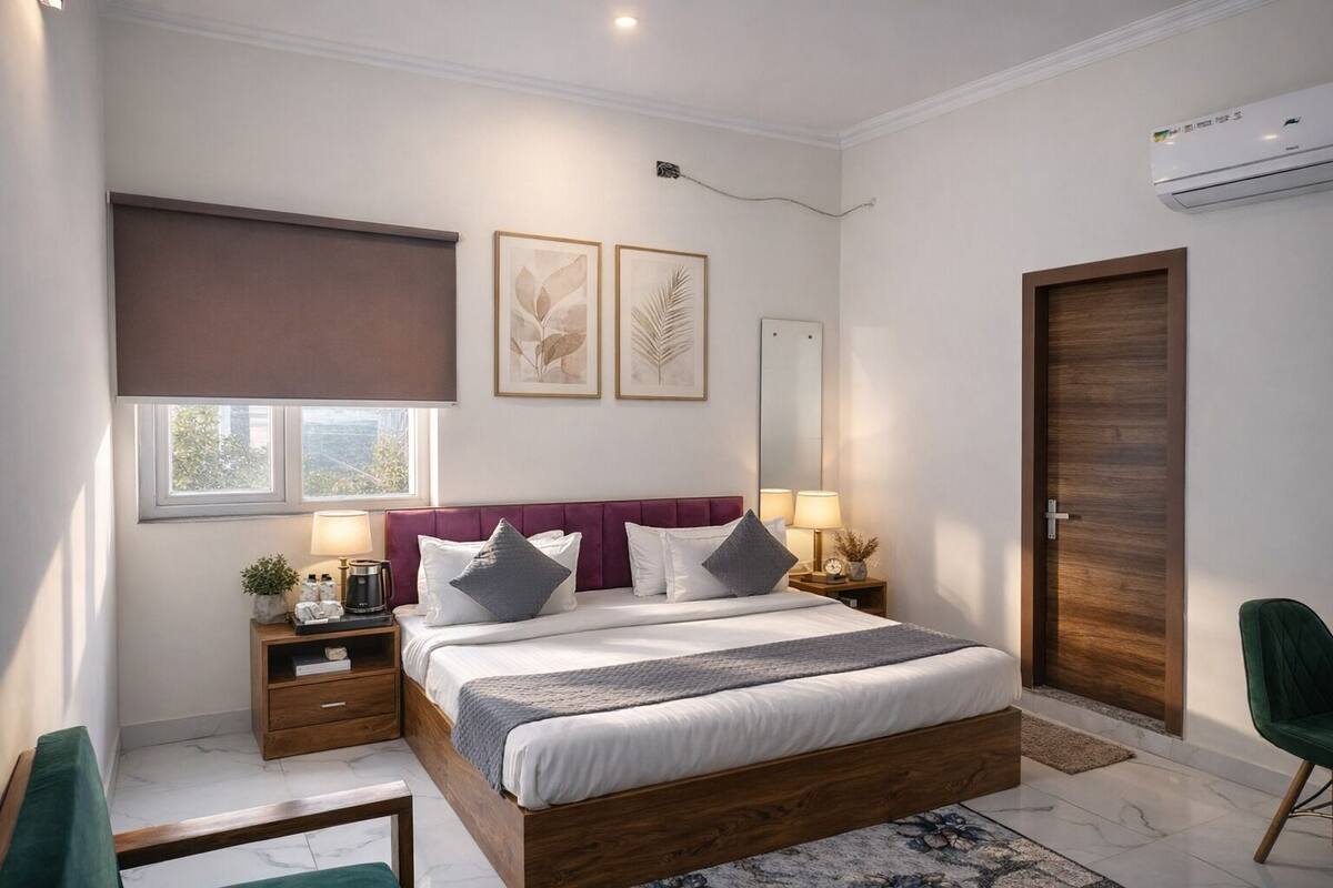 A modern bedroom with a wooden bed, two bedside tables, a nightstand, a green chair, a large mirror, and a window with a view.