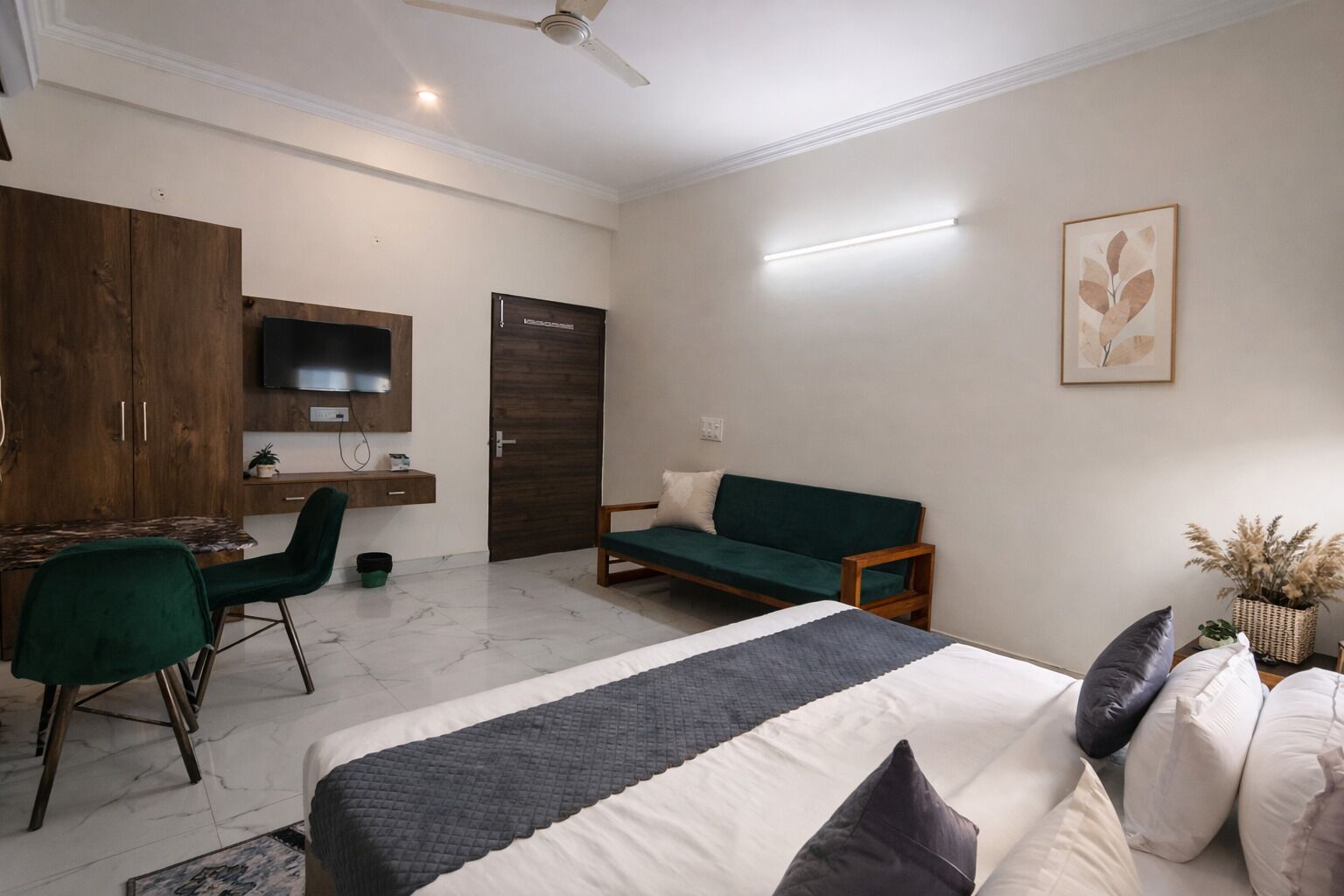 A bedroom with a bed, a desk, a chair, a sofa, and a television.